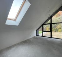 Ein Dachzimmer in einem Einfamilienhaus mit großen Fenstern und Blick auf den Wald.