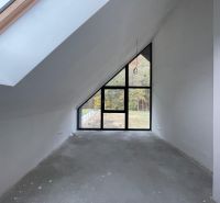 Ein Dachzimmer mit großen Fenstern und einer hervorstehenden Decke in einem Einfamilienhaus, ohne Bodenbelag.