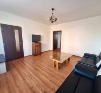 Wohnzimmer in einer 3-Zimmer-Wohnung mit Holzboden, schwarzem Sofa und Fernseher.