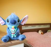 Ein Zimmer in einer 4-Zimmer-Wohnung mit gelben Wänden, Spielzeug und einem Bett mit einer rosa Überdecke.