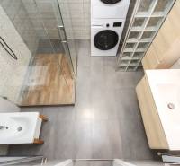 Badezimmer mit Waschmaschine und Duschkabine in einer 4-Zimmer-Wohnung, Boden mit Holzdekor.