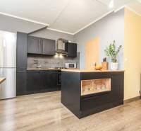 Küche in einer 4-Zimmer-Wohnung mit Insel, schwarzen Schränken und Boden in Holzoptik.