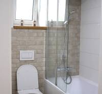 Badezimmer in einer 3-Zimmer-Wohnung mit Badewanne, Dusche, Toilette und dekorativer Wand in Ziegeloptik.