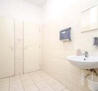 Büro mit Waschbecken, Spendern und Spiegel. Weiße Fliesen, heller Boden.