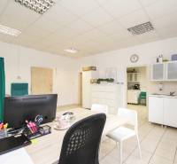 Ein Büro mit Möbeln, einem Computer und einer kleinen Küche, auf dem Boden sind Fliesen.