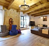 Innenraum einer Hütte mit Steinwand, großem Sofa und Boden in Holzoptik.