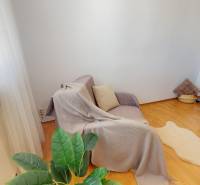 Ein Zimmer in einer 3-Zimmer-Wohnung mit einem Sofa, einem Tisch, einem dekorativen Teppich und einem Boden in Holzoptik.