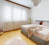 Helles Schlafzimmer mit großem Bett, Holzboden und durchsichtigen Vorhängen in einer 3-Zimmer-Wohnung.