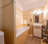 Badezimmer mit gelben Fliesen, Badewanne, Waschbecken und Stauraum in einer 4-Zimmer-Wohnung.