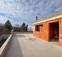 Ein im Bau befindliches Einfamilienhaus mit Terrasse auf einem großen Hof, umgeben von Natur und Bäumen.