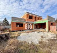 Unvollendeter Ziegel-Einfamilienhausbau, umgeben von Gras und Holzpaletten.