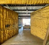 Geschäftsräume mit offenen Türen und einem Metalldach, im Hintergrund ist ein Auto zu sehen.