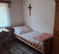 Einfaches Zimmer in einem Einfamilienhaus mit Holzmöbeln, Teppich und einem Kreuz an der Wand.