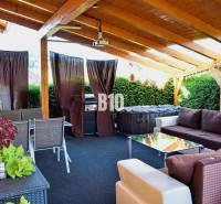 Die Terrasse des Einfamilienhauses mit Sitzgelegenheiten und Grill, teilweise überdacht mit einem Holzdach.