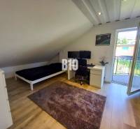 Dachzimmer mit Schreibtisch, Bett und Balkontür in einem Einfamilienhaus.