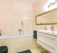 Badezimmer mit Spiegel, Badewanne und Waschbecken in einem Einfamilienhaus, helle Fliesen.