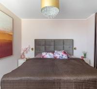 Schlafzimmer mit breitem Bett, dekorativen Kissen, Bild und verstecktem Stauraum in einer Vierzimmerwohnung.