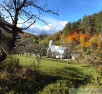 Herbst in den Gärten von Hlboké nad Váhom mit einer kleinen Kirche zwischen den Bäumen, bunte Wälder im Hintergrund.