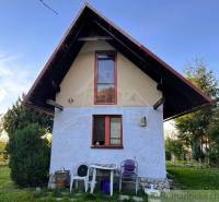 Hütte in Sološnica mit steilem Dach, Fenster, Natur und Plastikstühle.