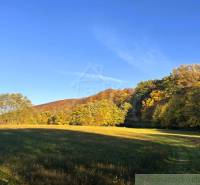 Herbstlandschaft bei Sološnica, mit bunten Bäumen am Hang und blauem Himmel.
