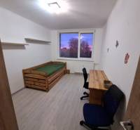 Ein Zimmer mit Bett und Tisch in einer 3-Zimmer-Wohnung, mit einem Boden in Holzoptik.