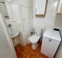 Badezimmer in einer Einzimmerwohnung mit Waschmaschine und WC, mit weißen Fliesen.