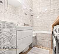 Ein Badezimmer in einer 3-Zimmer-Wohnung mit einer Badewanne, Fliesen und einem Boden in Holzoptik.