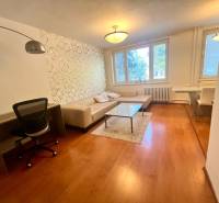 Obývací pokoj v třípokojovém bytě s pohovkou, stolkem a pracovním stolem.