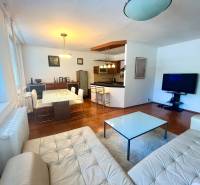 Wohnzimmer mit Küche in einer 3-Zimmer-Wohnung, Ausstattung umfasst ein Sofa, einen Tisch und einen Fernseher.