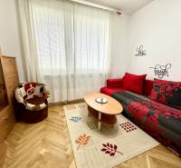 Ein Studio mit einem Boden in Holzoptik, einem roten Sofa und einem Sessel.