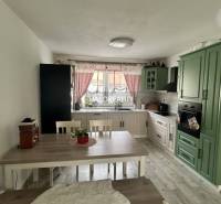 Küche in einem Einfamilienhaus mit grüner Küchenzeile, Esstisch und roten Vorhängen.