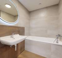 Badezimmer in einer 2-Zimmer-Wohnung mit Badewanne, Waschbecken und rundem Spiegel.