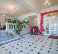 Hotelrezeption mit Pflanzen und Kronleuchtern, Fliesen mit geometrischem Muster.