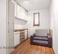 Ein Zimmer in einem Einfamilienhaus mit einem Boden in Holzoptik, einem grauen Sofa und Aufbewahrungsschränken.