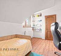 Ein Zimmer in einem Einfamilienhaus mit einem Bett, Regalen, einem Tisch und einem Boden mit Holzdekor.