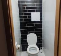 Eine Toilette mit schwarzen Fliesen in einer 3-Zimmer-Wohnung, ergänzt durch weiße sanitäre Ausstattung.