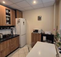 Küche in einer 3-Zimmer-Wohnung mit weißen Geräten, einem Boden in Holzoptik und Fenstern mit Jalousien.