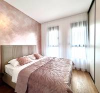 Schlafzimmer in einer Einzimmerwohnung mit rosa Wänden und einem Boden in Holzoptik.