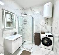 Badezimmer in einer Einzimmerwohnung mit Dusche, Waschmaschine und eleganten Marmorkacheln.