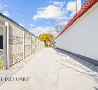 Eine schmale Zufahrtsstraße zwischen Einfamilienhäusern in Orechová Potôň, gesäumt von einer Mauer und Bäumen.