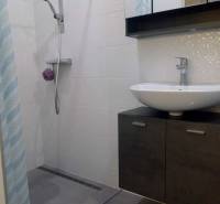 Badezimmer mit moderner Duschkabine in einer Einzimmerwohnung, helle Fliesen, Waschbecken.