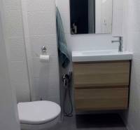 Kompaktes Badezimmer mit Waschbecken und Schrank in einer Einzimmerwohnung, Fliesen mit feiner Textur.