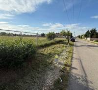 Straße in Miloslavov mit Grundstücken für Wohnbebauung und angrenzenden Grünflächen.