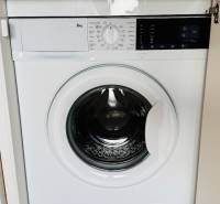 Eine eingebaute Waschmaschine in einer Einzimmerwohnung mit einem Boden in Holzoptik.