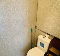 Toilette in einer Einzimmerwohnung mit Spülkasten und Wand mit Reliefmuster.