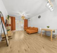 Wohnzimmer in einer Zweizimmerwohnung mit Holzboden, orangefarbenem Sofa und Esstisch.