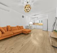 Wohnzimmer in einer 2-Zimmer-Wohnung mit einem orangefarbenen Sofa und einem Boden in Holzoptik.