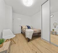 Schlafzimmer in einer 2-Zimmer-Wohnung mit Holzboden, weißem Stuhl und Kleiderschrank.