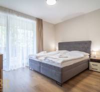 Schlafzimmer in einer 2-Zimmer-Wohnung mit hellen Vorhängen und einem Boden in Holzoptik.