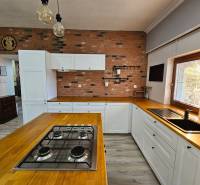 Eine Küche in einem Einfamilienhaus mit einer Ziegelwand, Holzelementen und einem Boden mit Holzdekor.